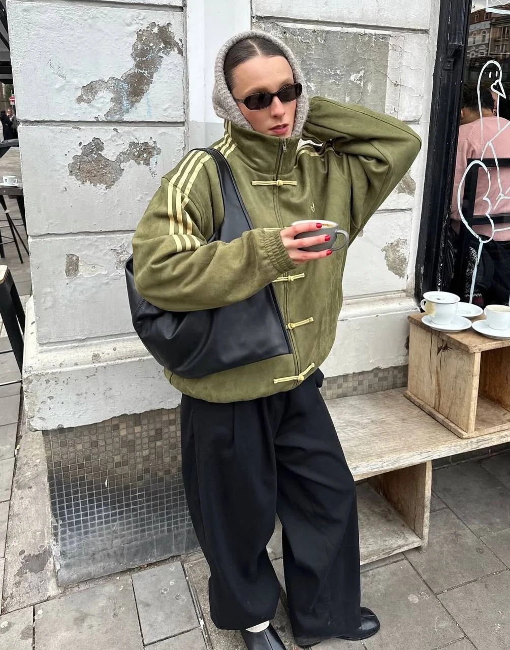 Оливковый Adidas Tang Jacket в городском образе: чёрные широкие брюки, кожаная сумка на плече, чашка кофе в руке
